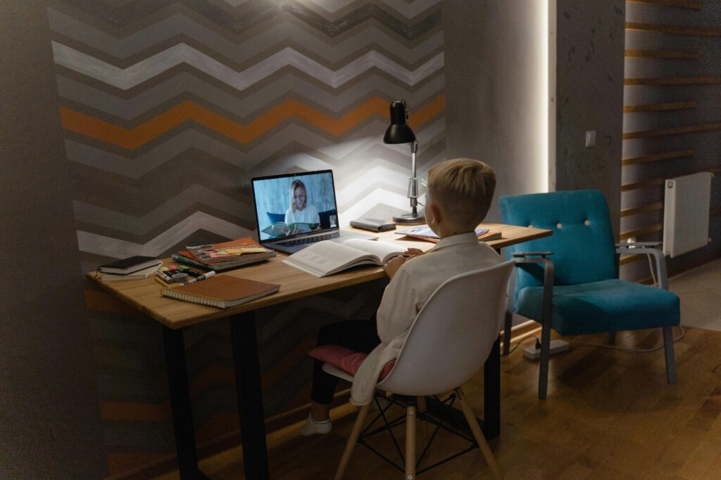 Young boy attending virtual class at home desk with laptop, focusing on education.